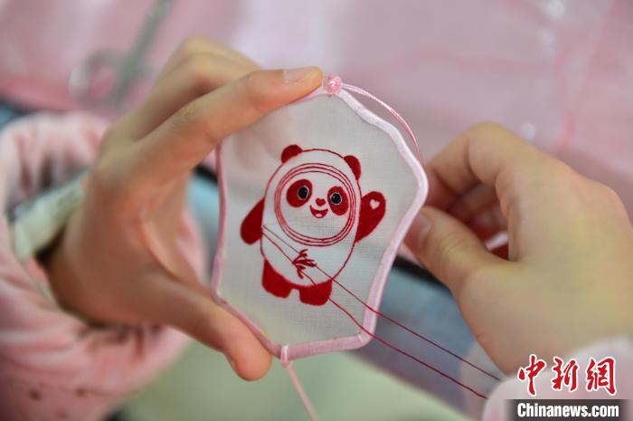 圖為一名小學生正在繡制2022年北京冬奧會吉祥物“冰墩墩”形象?！∮髟屏?攝