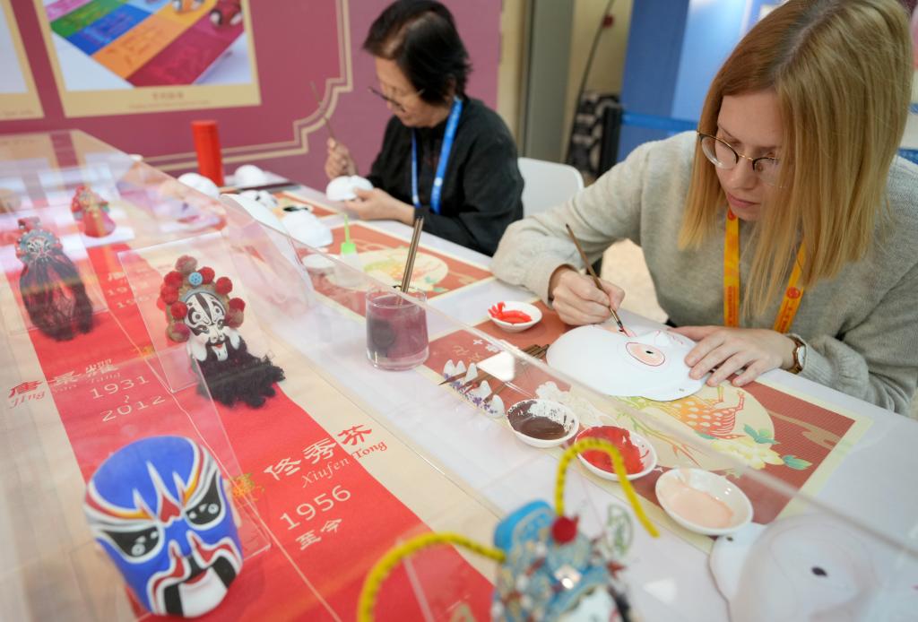 10月16日，在第三屆“一帶一路”國際合作高峰論壇新聞中心，來自比利時(shí)的記者（右）體驗(yàn)畫京劇臉譜。新華社記者 王毓國 攝