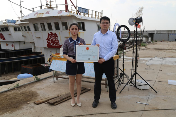 海鮮電商張夢琴與幫辦員手持食品經(jīng)營許可證合影。贛榆區(qū)委宣傳部供圖